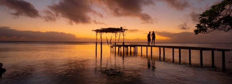 Silhouetted couple standing on wooden pier at sunset in Fakarava French Polynesia