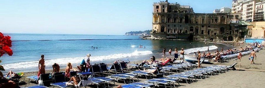 Beach loungers and umbrellas at Bagno Elena with historic building along the Naples coastline, Italy