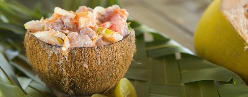Poisson cru served in a coconut bowl with fresh tuna, lime, and coconut milk on tropical leaves