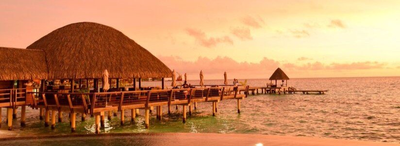 Overwater restaurant and wooden pier at sunset in Rangiroa with warm orange sky and calm ocean