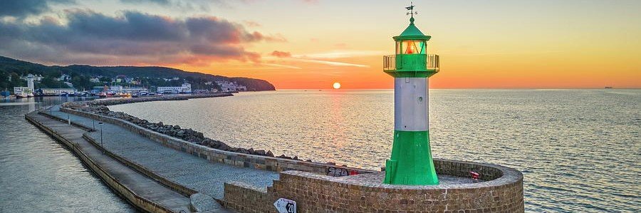 Green and white lighthouse at sunset in Sassnitz Rügen Germany overlooking the Baltic Sea harbor and pier.