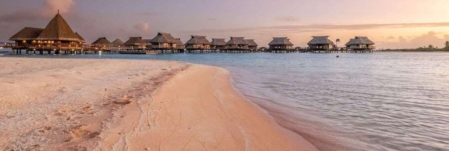 Pink sand beach at sunset with overwater bungalows and calm lagoon