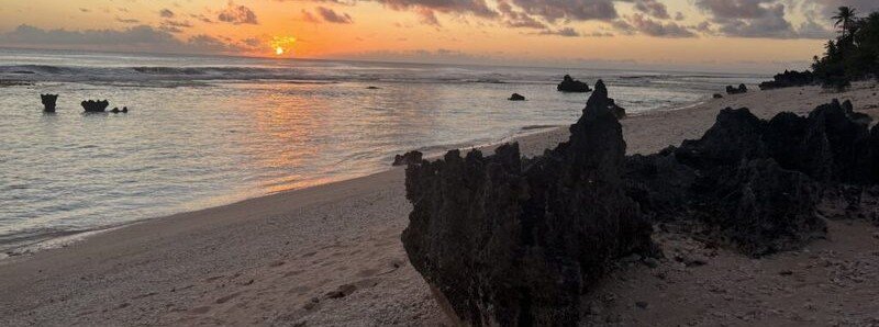 Sunset over lagoon with rocky coral formations and sandy beach in Tikehau