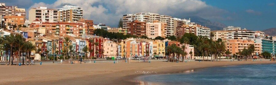 Colorful houses of Villajoyosa Spain along sandy beach with palm trees and Mediterranean coastline