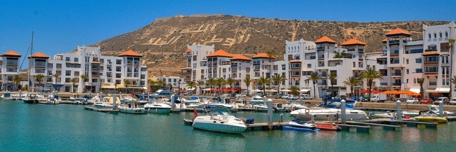 Agadir Marina with waterfront restaurants, boats, and mountain backdrop.