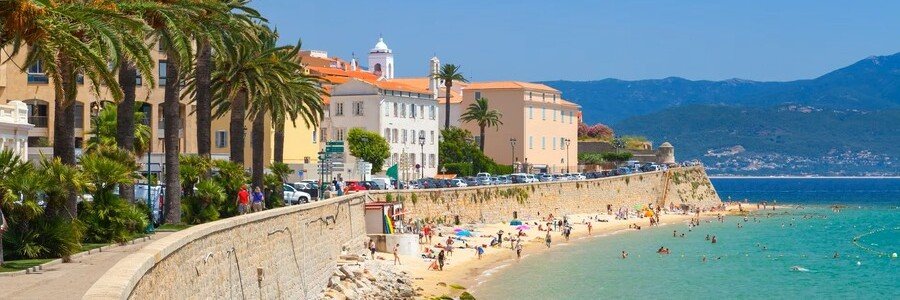 Ajaccio Corsica beach promenade with palm trees, turquoise water, and historic buildings along the coastline