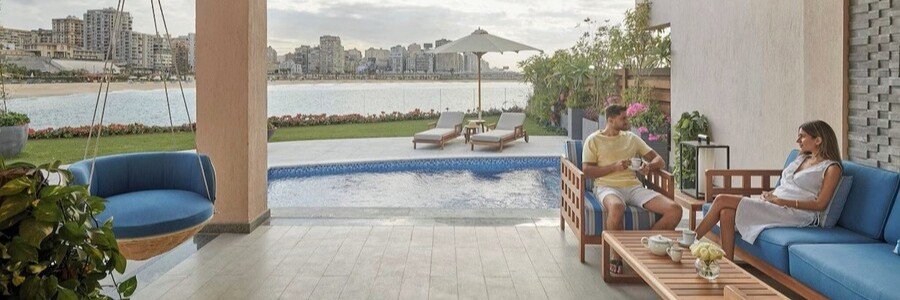 A man and woman relaxing on a luxury patio at the Four Seasons Hotel Alexandria, featuring a private pool and a view of the Alexandria Waterfront skyline and Mediterranean Sea.