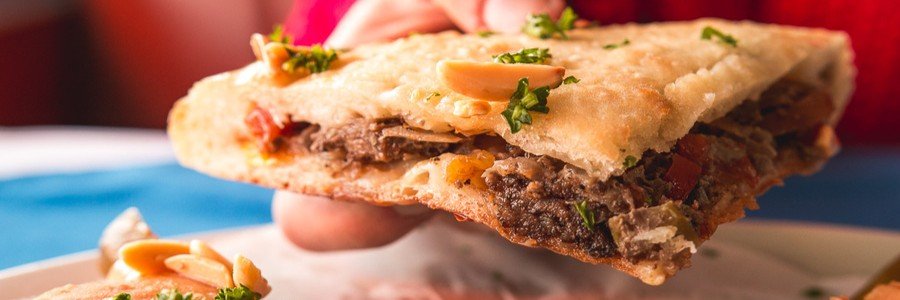 A close-up of a fresh slice of Alexandrian Hawawshi, showing the crispy baked dough and savory meat filling with herbs.