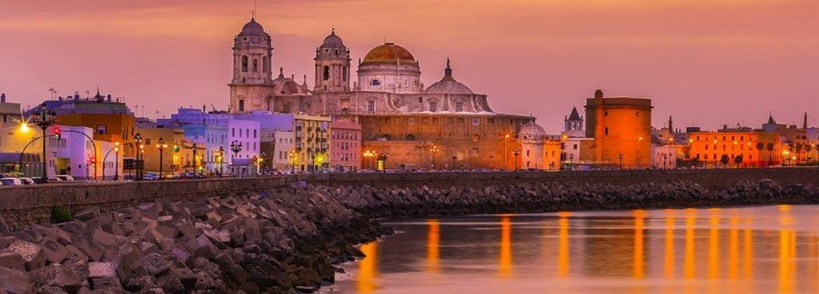 Cádiz Cathedral at sunset with golden dome and waterfront reflections along the coastline