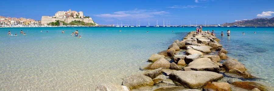 Calvi Beach Corsica with clear shallow water and view of the citadel in the distance