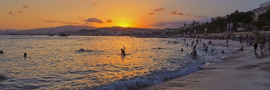 Sunset over Cannes beach with people swimming and golden light reflecting on the Mediterranean Sea