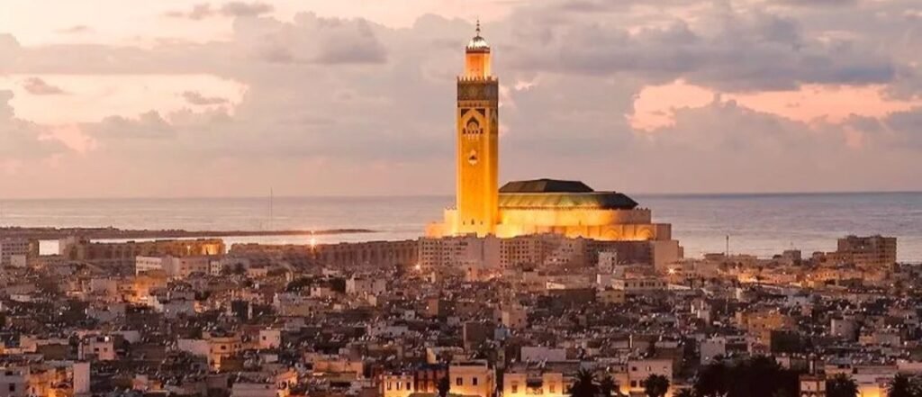 Sunset view over Casablanca Port and the city skyline with the illuminated Hassan II Mosque and the Atlantic Ocean in the background of Morocco.