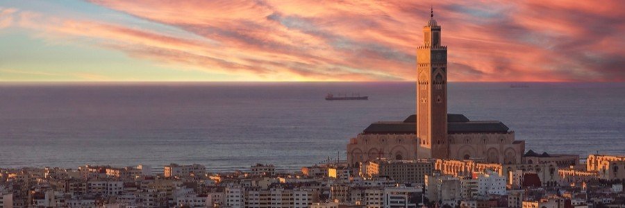 Sunset view over Casablanca Port and the city skyline with the illuminated Hassan II Mosque and Atlantic Ocean beyond.