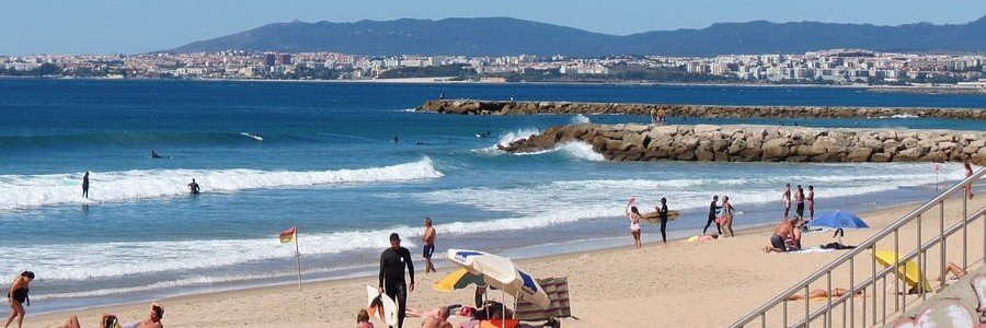 People surfing and relaxing on Caxias Beach near Lisbon with waves rolling in