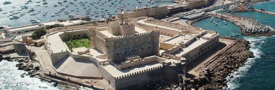 An aerial view of the stone Citadel of Qaitbay on the Alexandria Waterfront, showing the fort's walls, the harbor filled with boats, and the Mediterranean Sea.