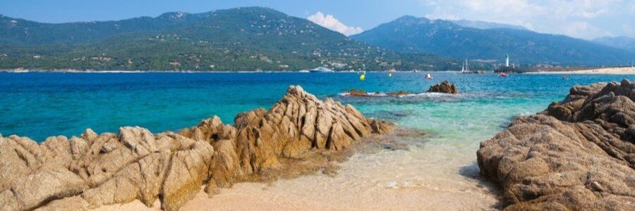 Corsica coastline with rocky shoreline, clear turquoise water, and mountains in the background