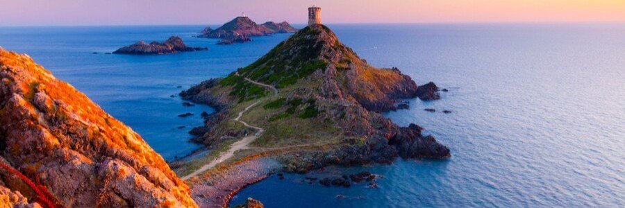 Corsica coastal view with rocky peninsula, tower, and sea at sunset