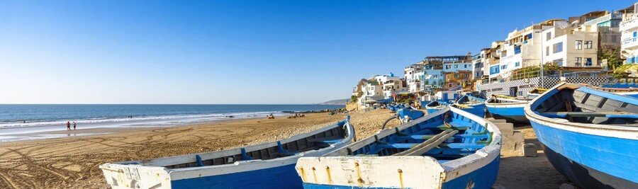 Coastal fishing village near Agadir with blue boats and sandy shoreline.