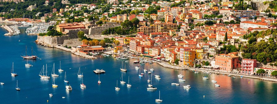 colorful harbor along the French Riviera with boats, hillside homes, and clear blue Mediterranean water