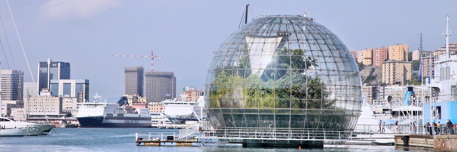 The glass Biosfera botanical garden at Porto Antico in Genoa, Italy, with cruise ships and city buildings in the background.