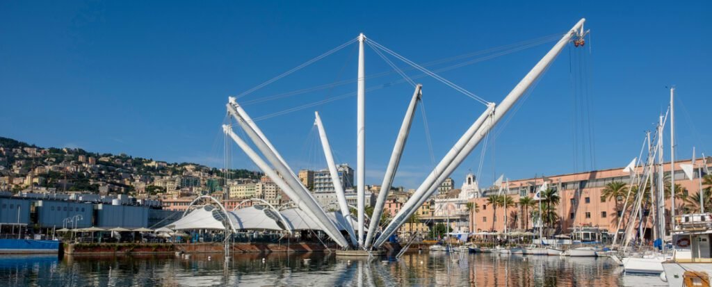 The Bigo panoramic lift and harbor at Porto Antico in Genoa, Italy, with sailboats and the city's hillside buildings in the background.