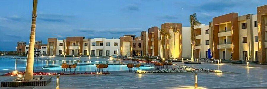 The modern multi-story buildings and illuminated outdoor swimming pools of the Helnan Port Fouad Resort under a deep blue evening sky.