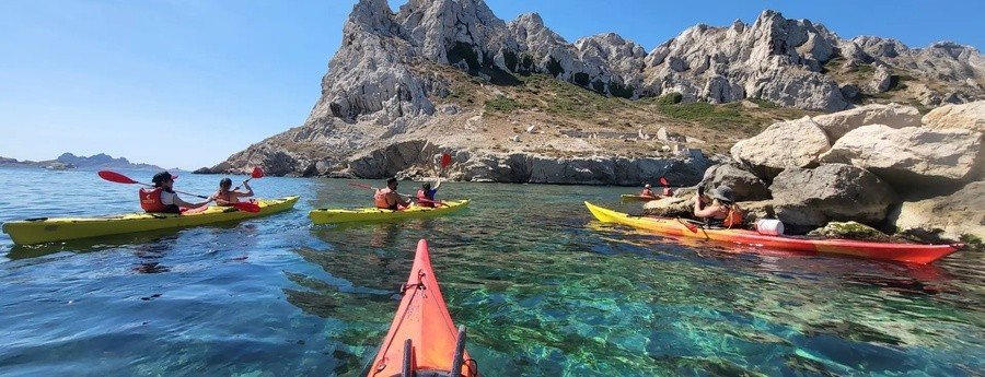 People kayaking in the Calanques near Marseille with clear turquoise water and rocky limestone cliffs