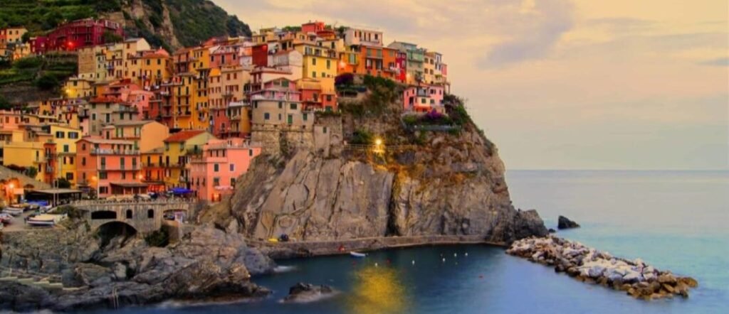 Manarola village in Cinque Terre at sunset, featuring colorful houses perched on a cliff overlooking the Ligurian Sea near La Spezia Port.