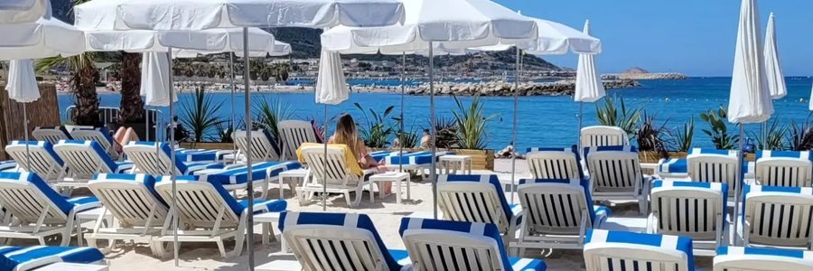 Les Voiles M beach club in Marseille with sunbeds, white umbrellas, and views of the Mediterranean coastline