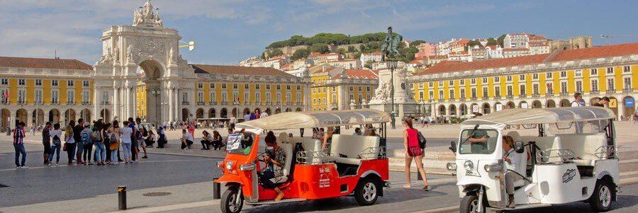 Colorful tuk tuks driving through Lisbon’s Commerce Square with historic arch and yellow buildings