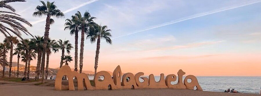 Malagueta Beach sign on the sandy shore in Malaga Spain with palm trees and sunset views