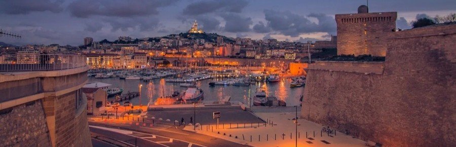 Vieux Port Marseille at sunset with glowing city lights and Notre-Dame de la Garde illuminated on the hill