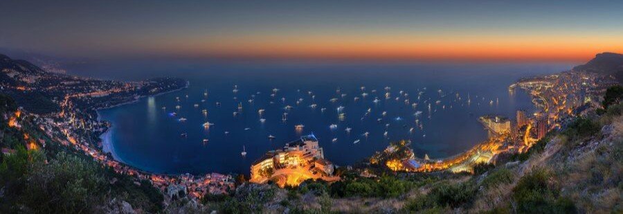Monaco coastline at sunset with harbor filled with yachts and city lights along the Mediterranean