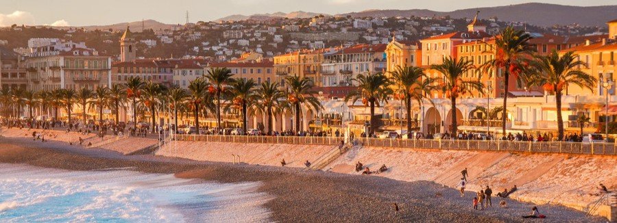 Nice Port and Nice Cruise Port near Promenade des Anglais beach with palm trees and colorful buildings at sunset