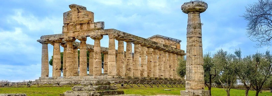 Three well-preserved ancient Greek temples with towering Doric columns standing in a green field under a clear blue sky.