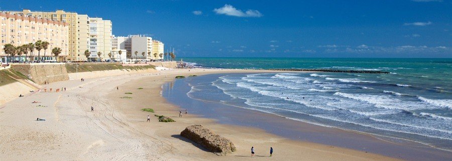 Playa de la Victoria in Cádiz with wide sandy beach, ocean waves, and promenade along the coastline
