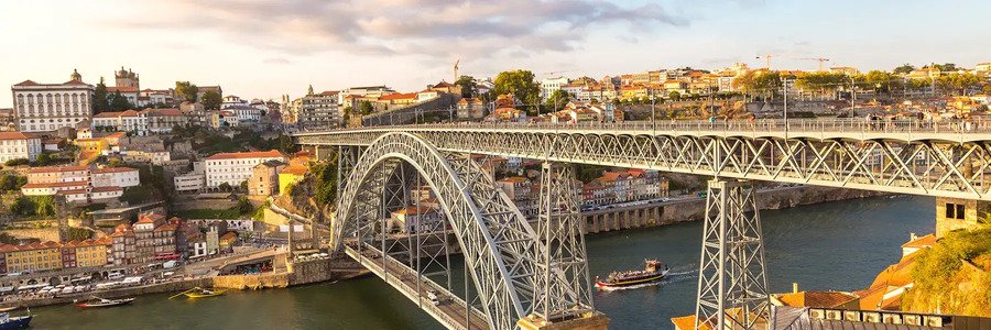 Wide view of the iron Dom Luís I Bridge over the Douro River in Porto, featuring the historic Ribeira District and traditional boats.