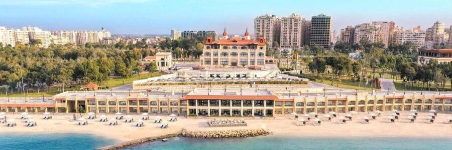 Aerial view of Rixos Montaza Alexandria beachfront resort with private beach, waterfront promenade, and city skyline along the Mediterranean coast in Egypt.