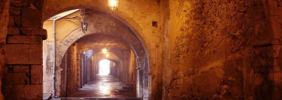 Rue Obscure stone tunnel passage with arched ceilings and warm lantern lighting in Villefranche-sur-Mer France