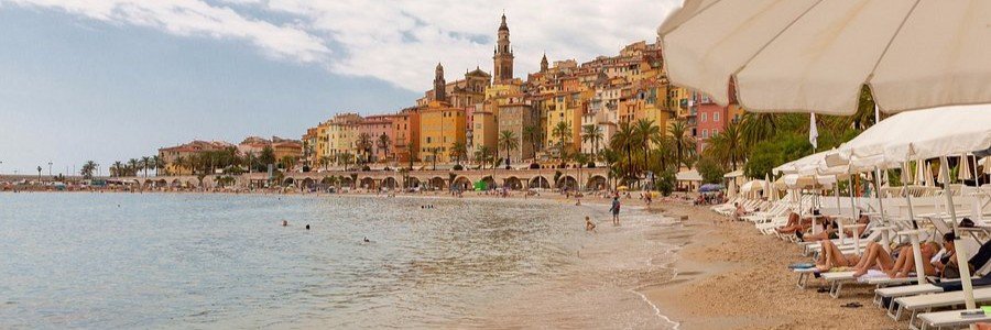 Sablettes Beach near Algiers Port with calm waters, sandy shore, and colorful waterfront buildings.