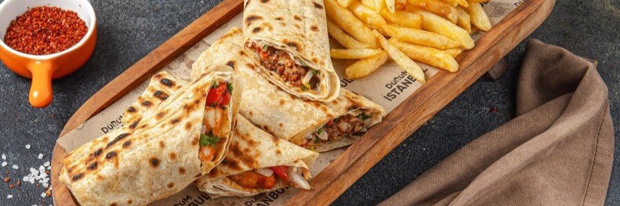 Turkish dürüm wrap with grilled meat and fries served on wooden board