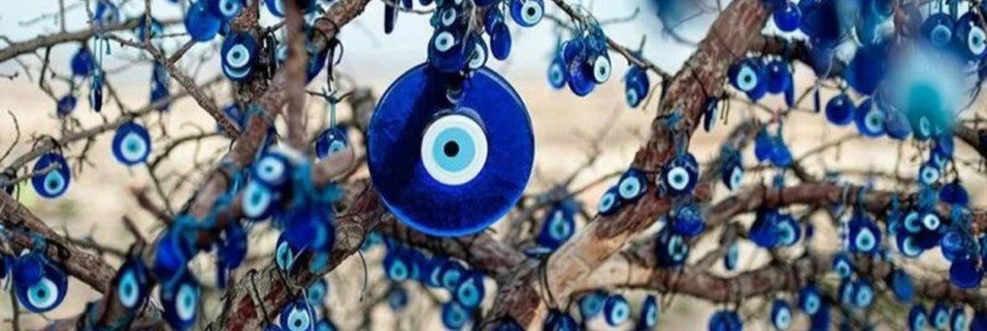 Close-up of a tree decorated with many blue glass Nazar amulets, or evil eye charms, hanging from its bare branches against a blurred natural background.