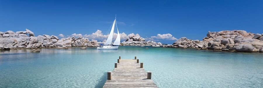 wooden pier leading into clear turquoise water with a sailboat in Villefranche bay on the French Riviera