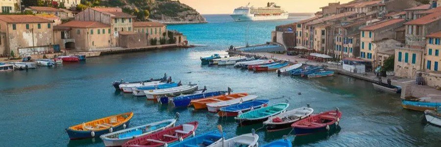 Small boats in Villefranche-sur-Mer port with waterfront buildings and cruise ship in the distance