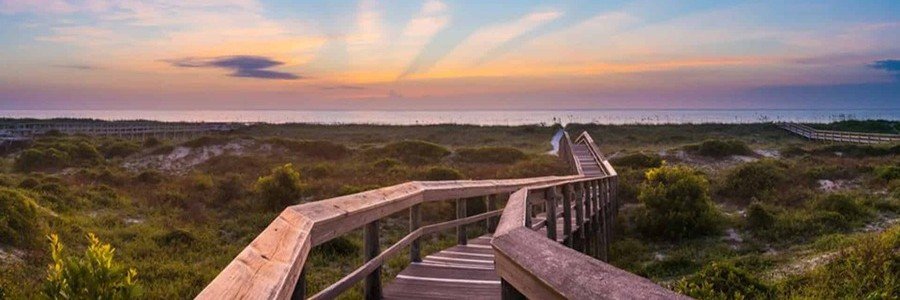 Wooden boardwalk leading through coastal dunes toward Fernandina Beach at sunset on Amelia Island, Florida.