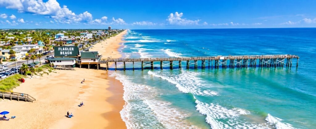 Aerial view of Flagler Beach Pier, golden sandy shoreline, and turquoise Atlantic Ocean along Florida's coast.