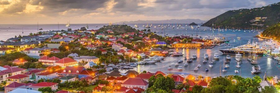 Gustavia Harbor illuminated at sunset with yachts and waterfront buildings.