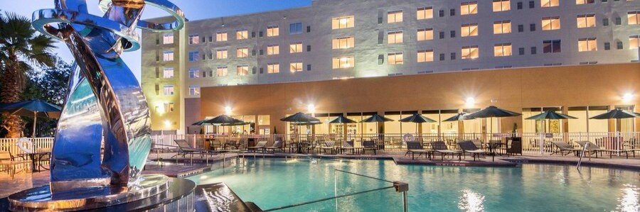 Evening view of the outdoor pool at Hyatt Place Cape Canaveral with lounge chairs and hotel in the background.