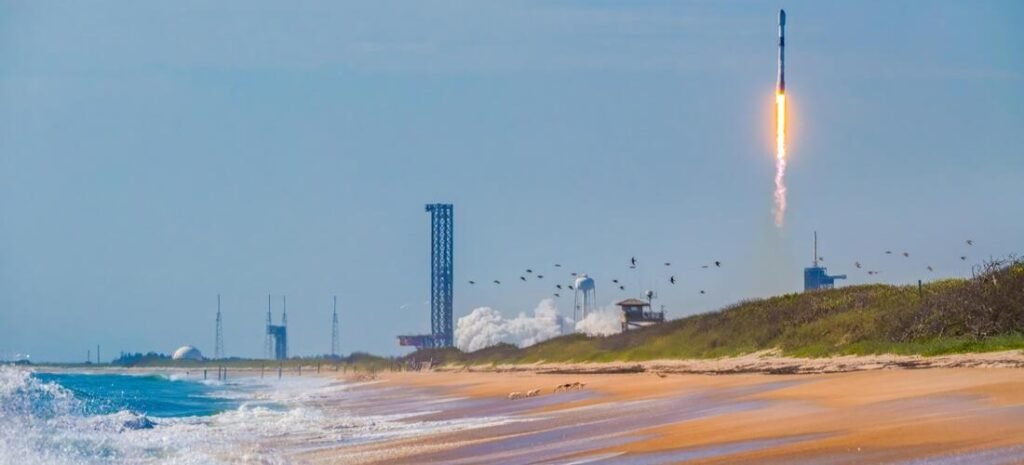 A SpaceX Falcon 9 rocket ascending into a clear blue sky over the ocean dunes at Playalinda Beach in Cape Canaveral Florida.