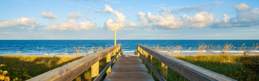 Wooden beach boardwalk leading to a pristine, uncrowded sandy shore and blue ocean in Satellite Beach, Florida.